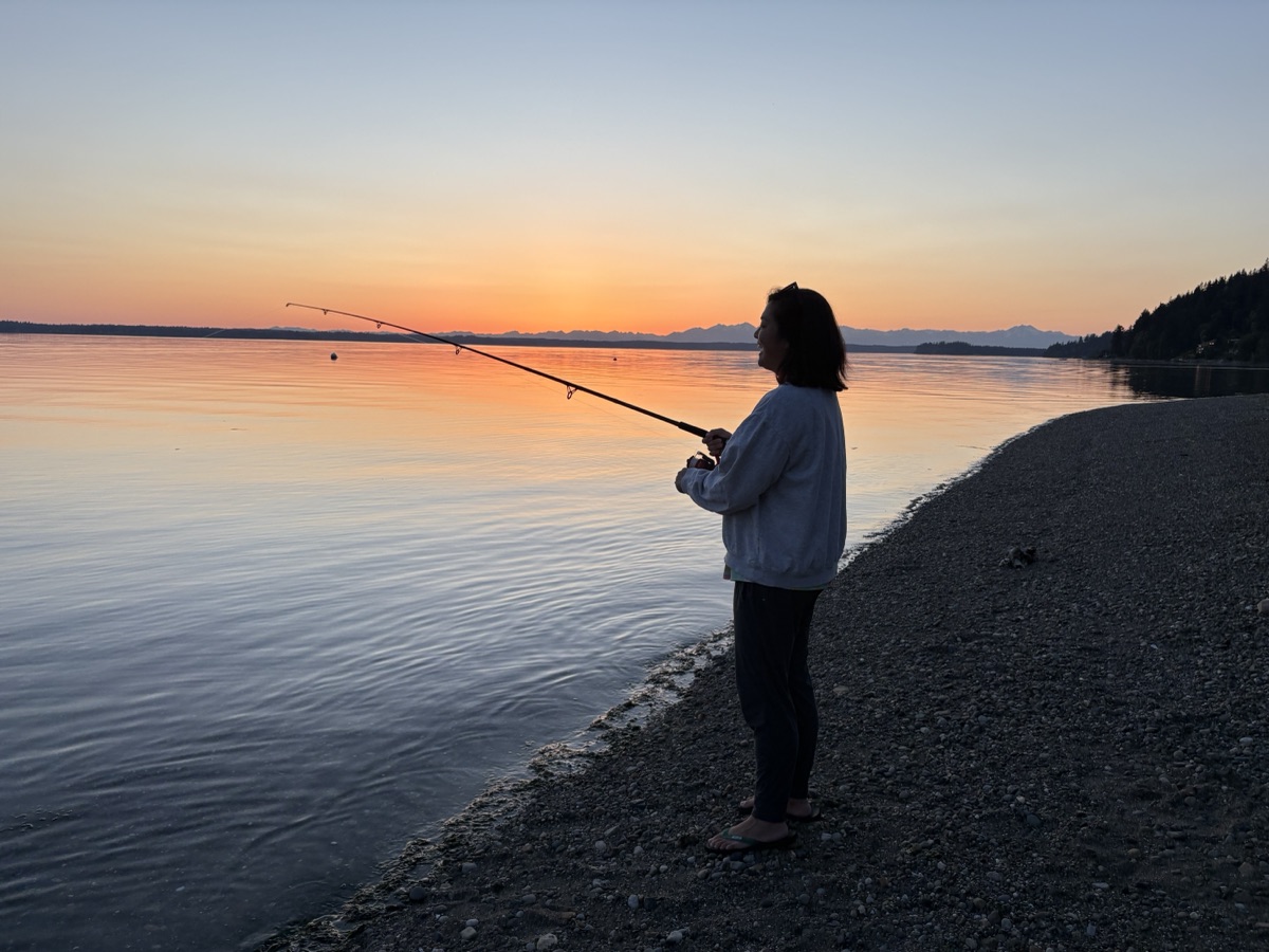 Kate casting a fishing line from a beach at sunset.